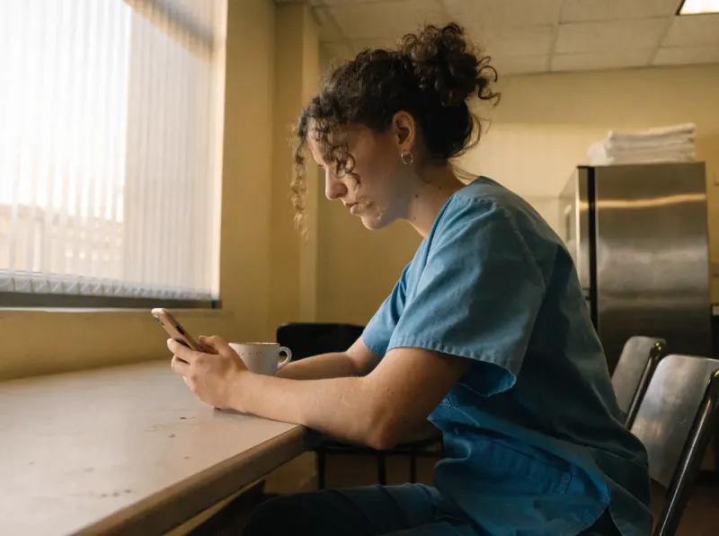 Pflegekraft im Pausenraum, ruhiger Moment mit dem Smartphone – anonymes Feedback in der Pflege